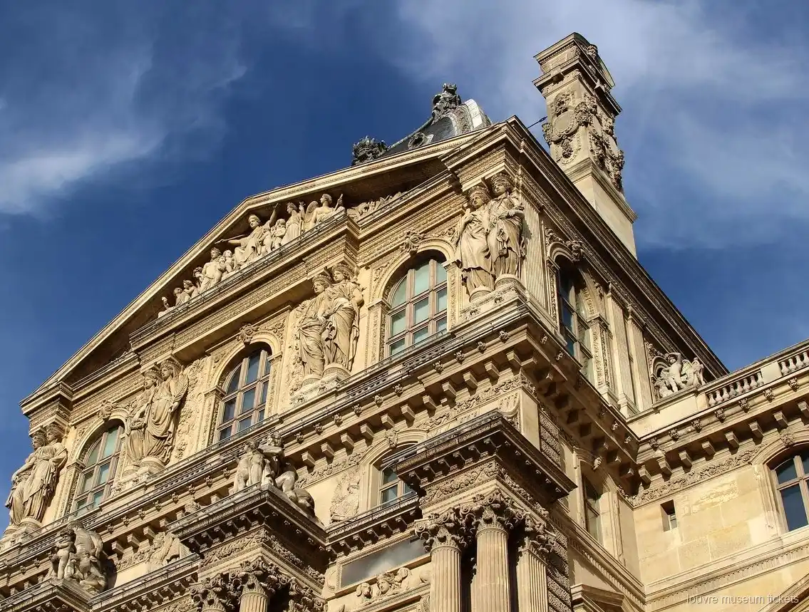 Façade sculptée du Louvre avec statues, fronton et colonnes sous un ciel bleu, vue avec des billets musée du Louvre