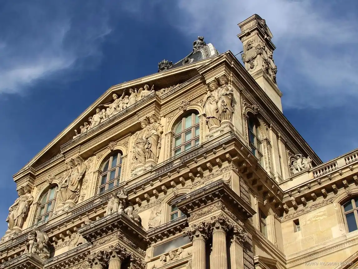 Fachada esculpida del Louvre con estatuas, frontón y columnas bajo cielo azul, vista con entradas Museo del Louvre