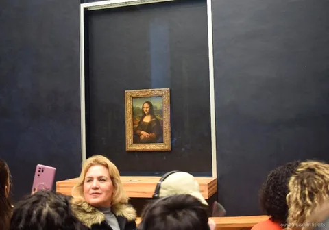 Besucher vor der Mona Lisa hinter Glas an der dunklen Saalwand, ein Höhepunkt der Führung mit Louvre Tickets