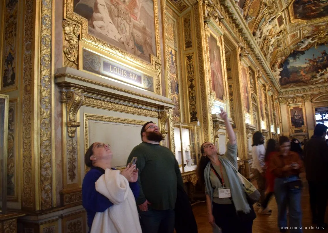 Lille gruppe kigger op på det malede, forgyldte loft i Apollon galleriet, en sal på turen med Louvre billetter