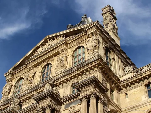 Udsmykket Louvre facade med skulpturer, gavl og søjler mod en dybblå himmel, set med Louvre billetter
