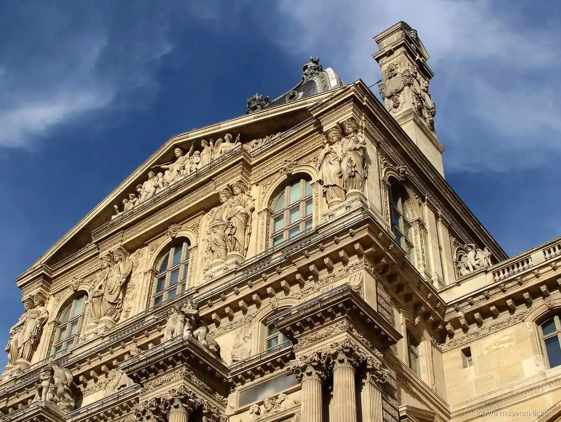 Gebeeldhouwde Louvre gevel met beelden, fronton en zuilen onder een blauwe lucht, gezien met Louvre museum tickets