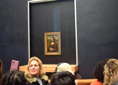 Besökare framför Mona Lisa bakom glas på salens mörka vägg, en höjdpunkt på visningen med biljetter till Louvren